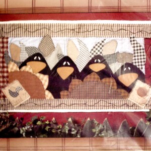 May include: A quilting pattern packet titled Crows in the Corn, #10217, featuring a finished size of 34 inches by 18 inches. The design displays four black crow figures with orange beaks, surrounded by checkered and patterned fabric patches.