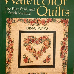 Könnte beinhalten: Ein Buch mit dem Titel Quick Watercolor Quilts: The Fuse, Fold, and Stitch Method von Dina Pappas. Das Cover zeigt einen dunkelgrünen Hintergrund und ein zentrales Quilt-Design mit einem Herzmuster aus rotem und orangem Rosenstoff.