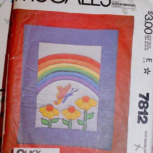 May include: A McCalls sewing pattern envelope for a quilt featuring a rainbow, a butterfly, and three yellow flowers. The design includes a red border and a purple inner frame. The text reads McCalls, Quick and Easy Quilts by Donna Lee, and 7812.