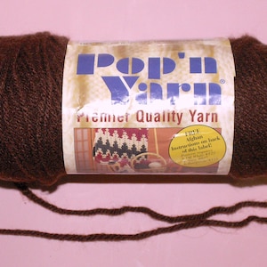 May include: A skein of dark brown yarn with a paper label that reads Pop'n Yarn Premier Quality Yarn. The label features a graphic of a crocheted blanket and a yellow circle with the text Free Afghan instructions on back of this label.