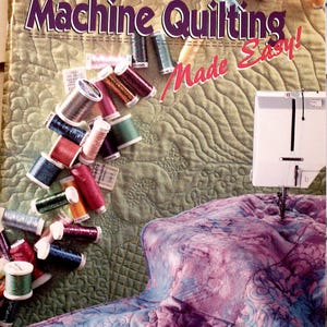 Puede incluir: Portada del libro "Machine Quilting Made Easy!" con un fondo acolchado verde. Carretes de hilo de varios colores están esparcidos por la portada. Una máquina de coser es visible a la derecha, con un edredón en progreso.