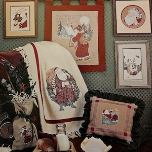 Puede incluir: Una colección de patrones de punto de cruz con Papá Noel. Los patrones se muestran en una variedad de superficies, incluyendo una almohada, una manta y un tapiz enmarcado. Los patrones son todos de estilo tradicional y presentan una variedad de colores, incluyendo rojo, verde y blanco. El texto "Here Comes Santa Claus" se muestra en la parte superior de la imagen. El texto "Designs by Carol Bryan and Ginny Fraser" se muestra en la parte inferior de la imagen.