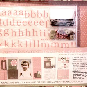 Op de afbeelding: Een scrapbookkit in een doos met roze en witte accenten. Inclusief alfabetstickers, knopen, linten en voorgesneden papierindelingen. De kit maakt een album van 20 cm x 20 cm. De tekst zegt "Scrapbook in a Box".