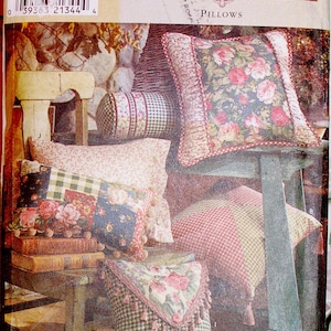 Puede incluir: Patrón de cojines Simplicity Home. La imagen muestra una variedad de cojines con diseños florales y de cuadros. Los cojines son en tonos rosa, verde y blanco. Algunos cojines tienen borlas y volantes. El número de patrón es 8044.