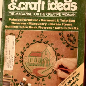 May include: A vintage magazine cover titled "decorating & craft ideas" with a green background. The cover features a painted wooden panel with a house design and the text "Special 28-Page Needlework Section".