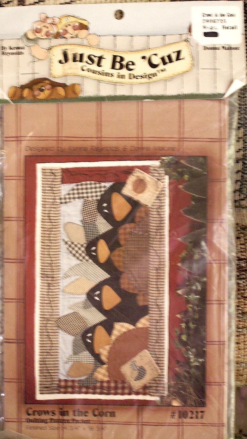 K&ouml;nnte beinhalten: Ein Quilt-Musterpaket mit dem Titel Crows in the Corn von Just Be Cuz Cousins in Design. Die Verpackung zeigt eine grafische Illustration von schwarzen Kr&auml;henformen mit orangefarbenen Schn&auml;beln, die vertikal vor einem karierten Hintergrund angeordnet sind.
