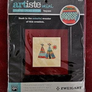 May include: A counted cross-stitch kit featuring a colorful design of two teepees with a sun. The kit is titled "artiste mini Teepees" and is designed by "Kooler Design Studio".