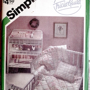 May include: Vintage Simplicity sewing pattern envelope featuring a nursery scene. The image shows a crib with a quilted blanket and pillow, a changing table, and a framed floral print. The envelope has the text "Simplicity" and "Tricia Guild".