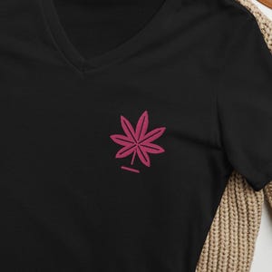 May include: Black v-neck t-shirt with a pink stylized leaf design.