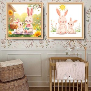 Op de afbeelding: Twee ingelijste prints van cartoon konijnen met een witte achtergrond. De bovenste print toont een moederkonijn en een babykonijn die in een bloemenveld zitten. De onderste print toont twee konijnen die in een bloemenveld zitten met een zon die erboven schijnt.