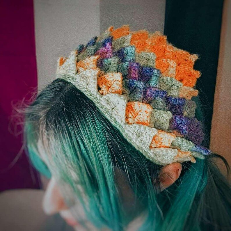 K&ouml;nnte beinhalten: Eine bunte H&auml;kelm&uuml;tze mit einem einzigartigen, strukturierten Design. Die M&uuml;tze ist aus verschiedenen Farben gefertigt, darunter Orange, Gr&uuml;n, Lila und Gelb.