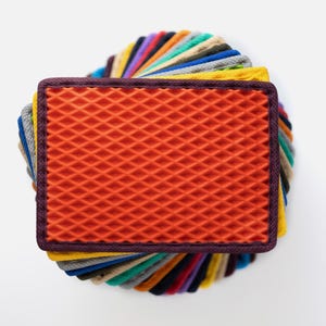 May include: A stack of fabric swatches in various colours and textures, including orange, yellow, green, blue, purple, and grey. The top swatch is a bright orange with a diamond pattern.