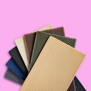 Könnte beinhalten: Eine Auswahl rechteckiger Matten in verschiedenen Farben, darunter Beige, Braun, Grün und Blau. Jede Matte hat ein strukturiertes, geometrisches Muster. Die Matten sind vor einem rosa Hintergrund angeordnet, um ihre vielfältigen Farbtöne und Designs hervorzuheben.