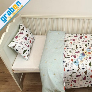 May include: A white crib with a light blue and white patterned duvet cover and a pink and white patterned pillow. The duvet cover features a whimsical design with dinosaurs, trees, and other nature-inspired elements.