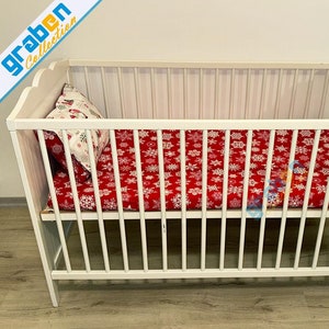 May include: White wooden baby crib with a red and white snowflake patterned sheet and a white pillow with a red and white snowflake design.