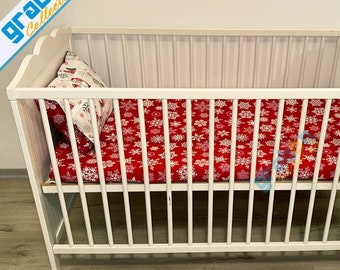 May include: White wooden cot with a red and white snowflake patterned sheet and a white pillow with a red and white snowflake design.