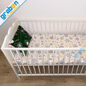 May include: White wooden baby crib with a snowflake patterned sheet and a green pillow with a snowman design.