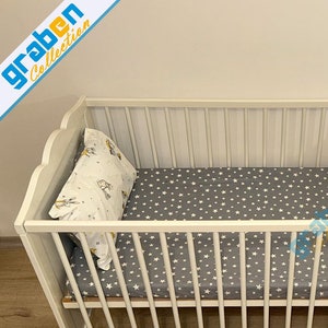 May include: White wooden baby crib with a gray and white star patterned fitted sheet and a white pillow with a gray and white animal print.