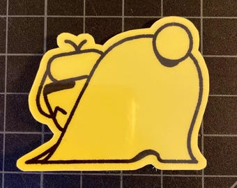 May include: A yellow sticker with a black outline. The sticker features a cartoon-style design of a creature with a rounded body and a small, detailed head. The sticker is on a black grid background.