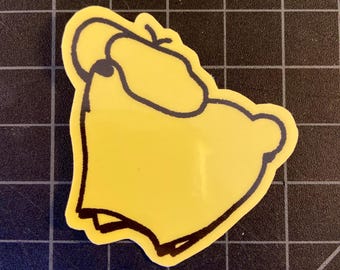 May include: A yellow sticker with a black outline depicting a cartoon character. The sticker has a glossy finish and is placed on a black surface with a grid pattern.