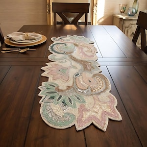 May include: A long, narrow table runner featuring intricate beadwork in soft pastel shades of pink, sage green, and cream. The design consists of organic, swirling floral and leaf-like shapes with a textured, shimmering finish laid flat.