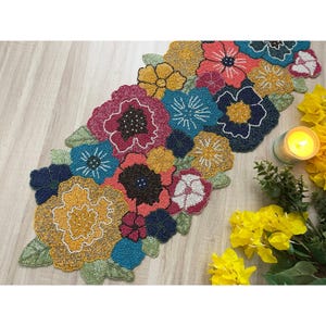 May include: A beaded table runner with a floral design. The runner features a variety of colors, including red, pink, yellow, blue, and green. The beads are arranged in a pattern that creates a realistic flower design.