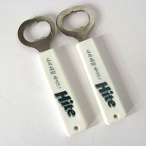 May include: Two bottle openers with a silver metal opener and a white handle. The handle has the word "Hite" in green and black, along with text in a foreign language. The openers are on a white background.