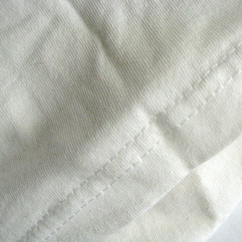K&ouml;nnte beinhalten: Nahaufnahme einer wei&szlig;en Stoffnaht mit einem geraden Stich. Der Stoff ist glatt und hat eine subtile Textur.