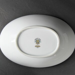 Puede incluir: Plato de servir ovalado blanco con un logotipo de Noritake China en oro y azul. El logotipo incluye el texto "Noritake China" y "Japan" y un escudo con la letra "N".