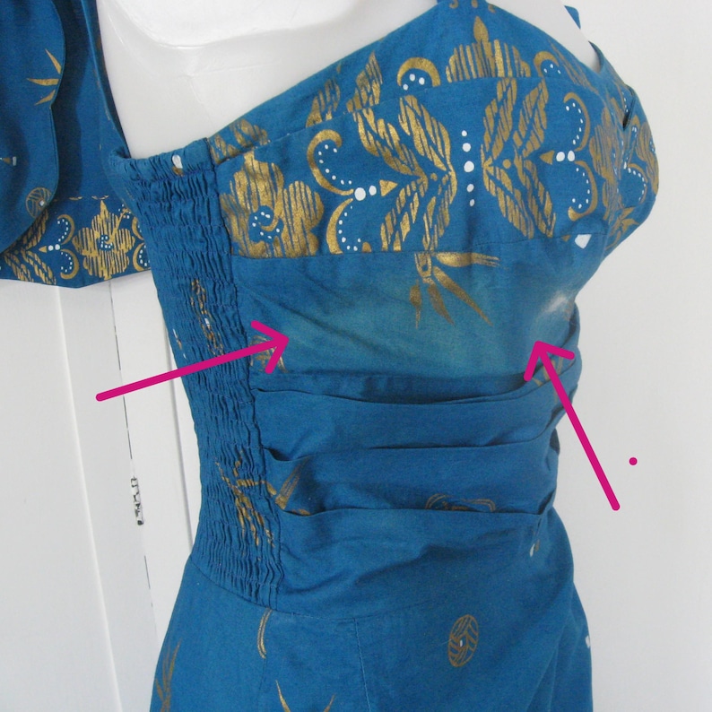 May include: A teal dress with gold floral and bamboo leaf patterns. The dress has a fitted bodice with shirring and a gathered waist. The fabric has a subtle ombre effect. The dress is sleeveless with a scoop neckline.