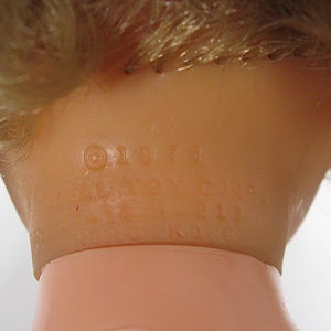 May include: A light-skinned doll neck featuring molded blonde hair and embossed text that reads &copy; 1974 IDEAL TOY CORP. HONG KONG. The plastic surface is smooth and flesh-toned, showing the manufacturer details clearly on the back of the doll head.