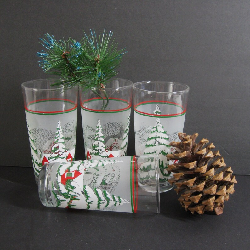 May include: Set of four frosted glass tumblers with a winter scene design. The glasses feature a red and green band around the top and a snowy landscape with trees and houses.