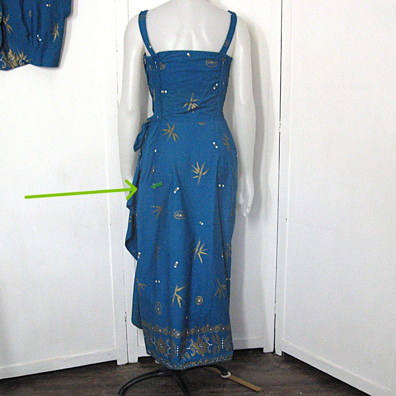 May include: A teal dress with spaghetti straps and a wrap-style skirt. It has gold leaf and dot patterns, and a decorative hem border. The dress is displayed on a mannequin. The dress is approximately 100 cm in length.