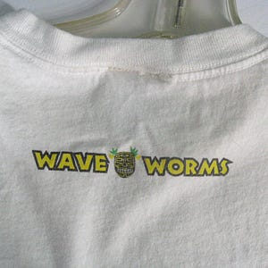 May include: White t-shirt with a yellow and black graphic that says "WAVE WORMS" with a tiki mask in the middle.