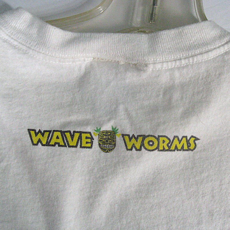 May include: White t-shirt with a yellow and black graphic that says "WAVE WORMS" with a tiki mask in the middle.