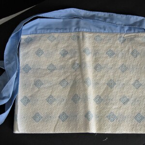 May include: A white fabric bag with a blue trim and a repeating pattern of blue squares. The bag has a long blue strap.