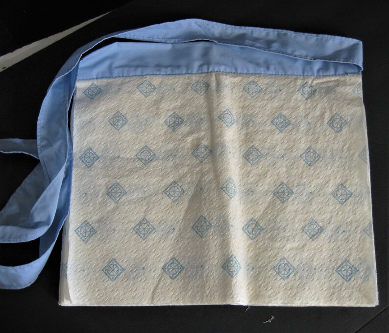 May include: A white fabric bag with a blue trim and a repeating pattern of blue squares. The bag has a long blue strap.