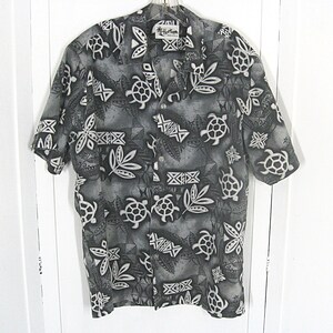 May include: A short-sleeved button-down shirt in shades of gray, black, and white. The fabric features a repeating pattern of sea turtles, tropical leaves, and geometric tribal motifs. The shirt has a collar and a front button closure.