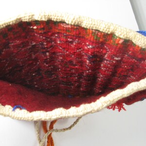 May include: Open view of a handmade pouch with a red interior and a cream-colored crocheted border. The interior features a patterned design with red, green, and black threads. Blue and orange threads are visible.