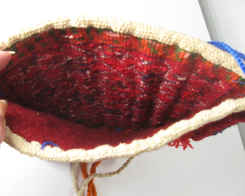 May include: Open view of a handmade pouch with a red interior and a cream-colored crocheted border. The interior features a patterned design with red, green, and black threads. Blue and orange threads are visible.