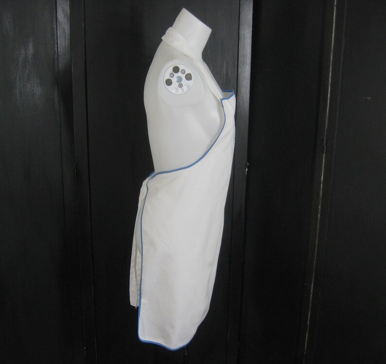 May include: White apron with a blue trim. The apron is hanging on a mannequin.