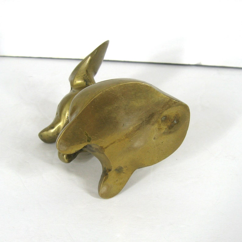 May include: A solid brass sculpture of a rabbit sitting on its haunches. The sculpture is a solid piece of metal with a smooth, polished finish.