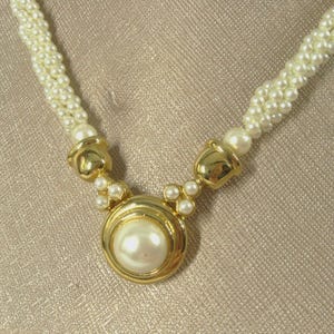 May include: A gold necklace with a large faux pearl pendant and a multi-strand pearl chain.
