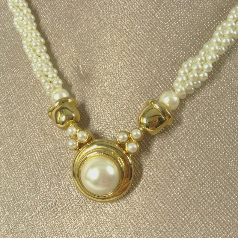 May include: A gold necklace with a large faux pearl pendant and a multi-strand pearl chain.