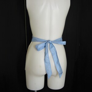 May include: A white mannequin wearing a light blue apron tied in a bow at the back.