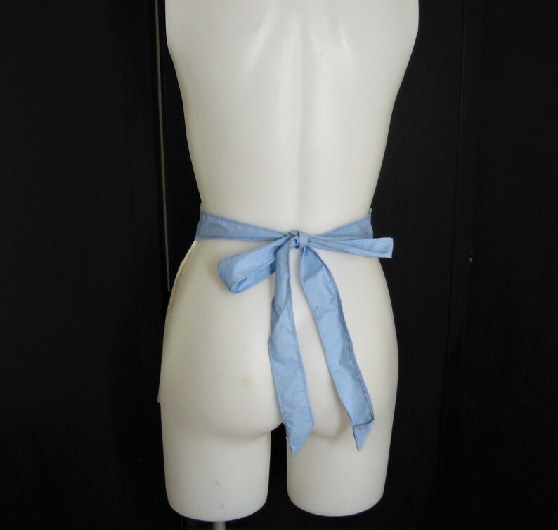 May include: A white mannequin wearing a light blue apron tied in a bow at the back.