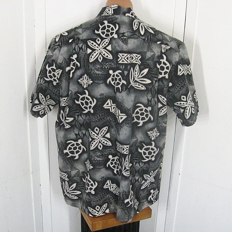 May include: A short-sleeved button-down shirt in shades of gray, black, and white. The fabric features a repeating pattern of sea turtles, stylized floral shapes, and geometric tribal-inspired motifs across the entire garment surface.