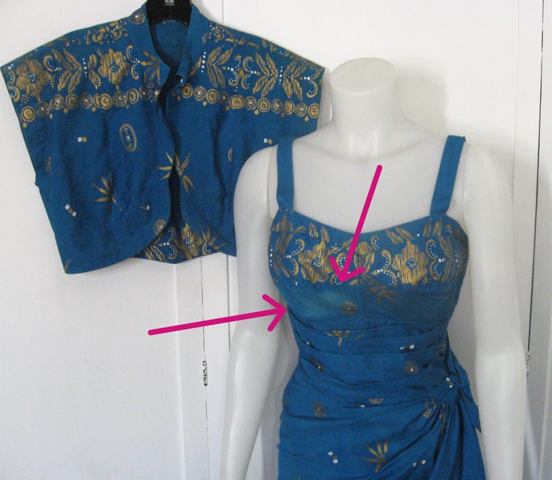 May include: A teal two-piece outfit comprising a sleeveless dress and a matching bolero jacket. The dress has a fitted bodice and a draped skirt. Both items are decorated with gold floral and geometric patterns.