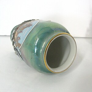 Pode incluir: Um pequeno vaso de cer&acirc;mica verde com borda dourada e interior branco. O vaso apresenta um painel decorativo com uma cena de paisagem. O vaso tem cerca de 10 cm de altura.
