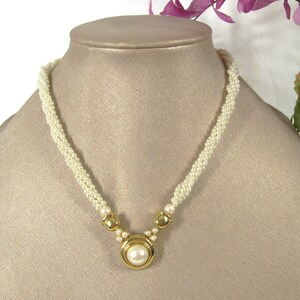 May include: A white pearl necklace with a gold pendant featuring a large pearl. The necklace is made of small, round pearls and has a simple, elegant design.